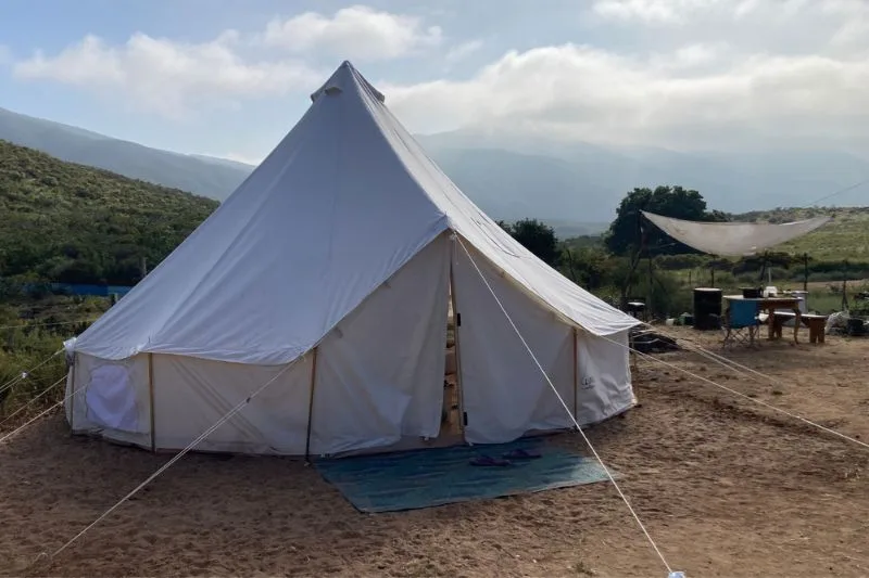 white bell tent with table and chairs on the right and mountains in the background.