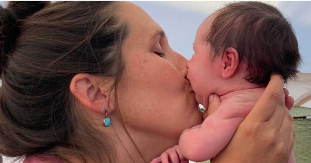 close up profile of woman kissing newborn on mouth.