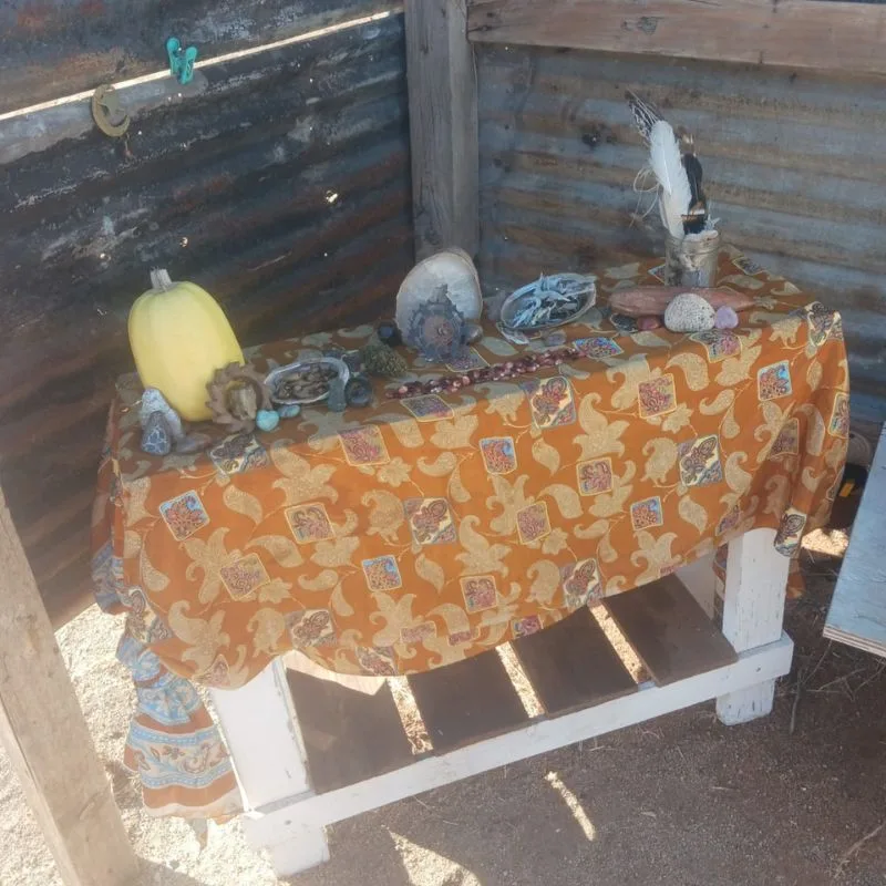 autumn alter, side table with printed fabric tablecloth with squash, feathers and sage in shell.