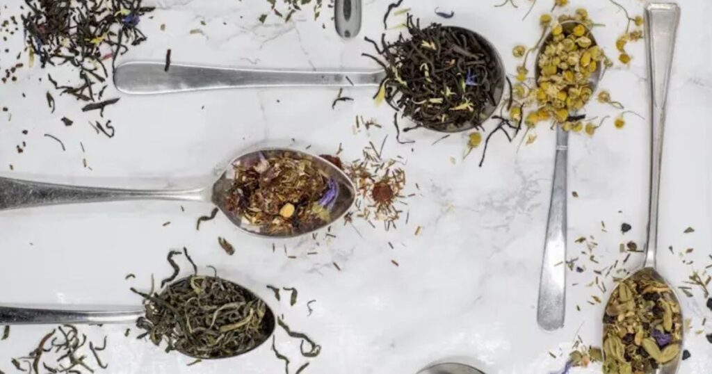 overhead view of dried herbs in spoons on white tabletop.