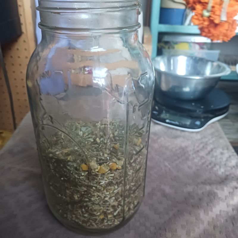 large glass mason jar filled half way with dry herbs. stainless steel bowl on scale in background.