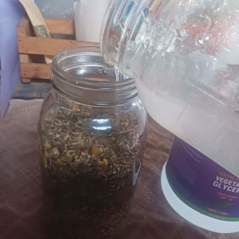 pouring glycerin into glass mason jar filled with herbs.