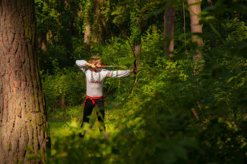 man doing archery in forest.