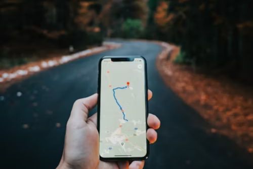 hand holding mobile phone with map on screen and winding road in background.