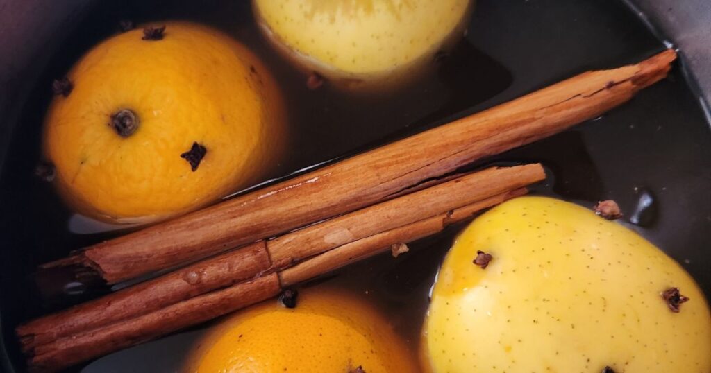 apples and oranges studded with whole cloves and whole cinnamon sticks floating in Wassail Punch in a pot.