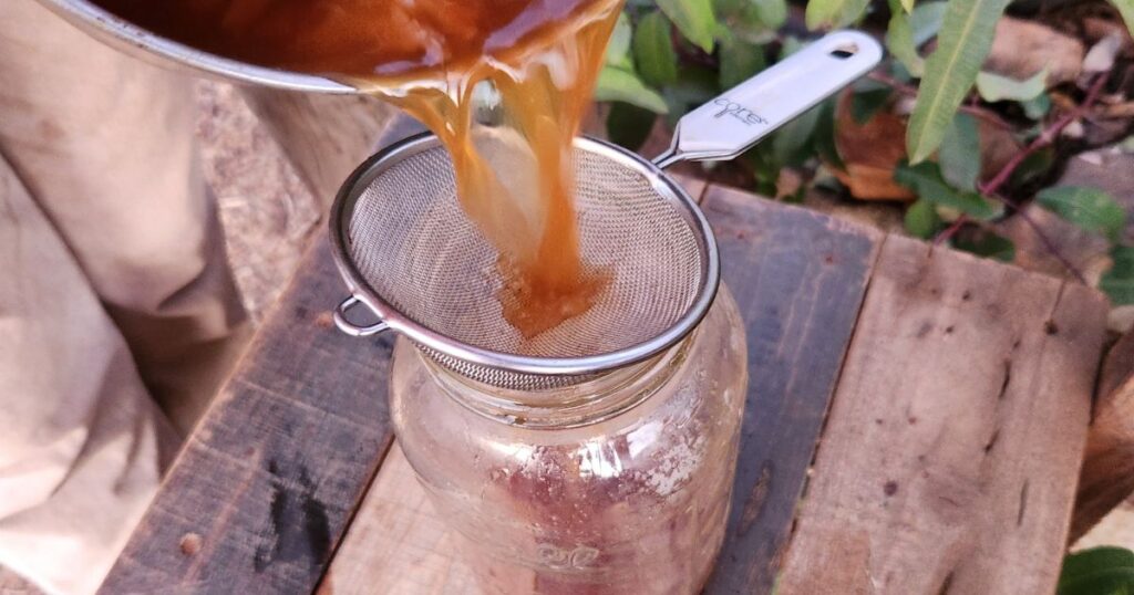 Wassail Punch being poured from a pot into a mason jar through a strainer.