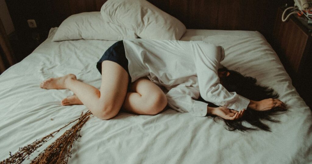 woman on unmade bed curled up with arms over face.