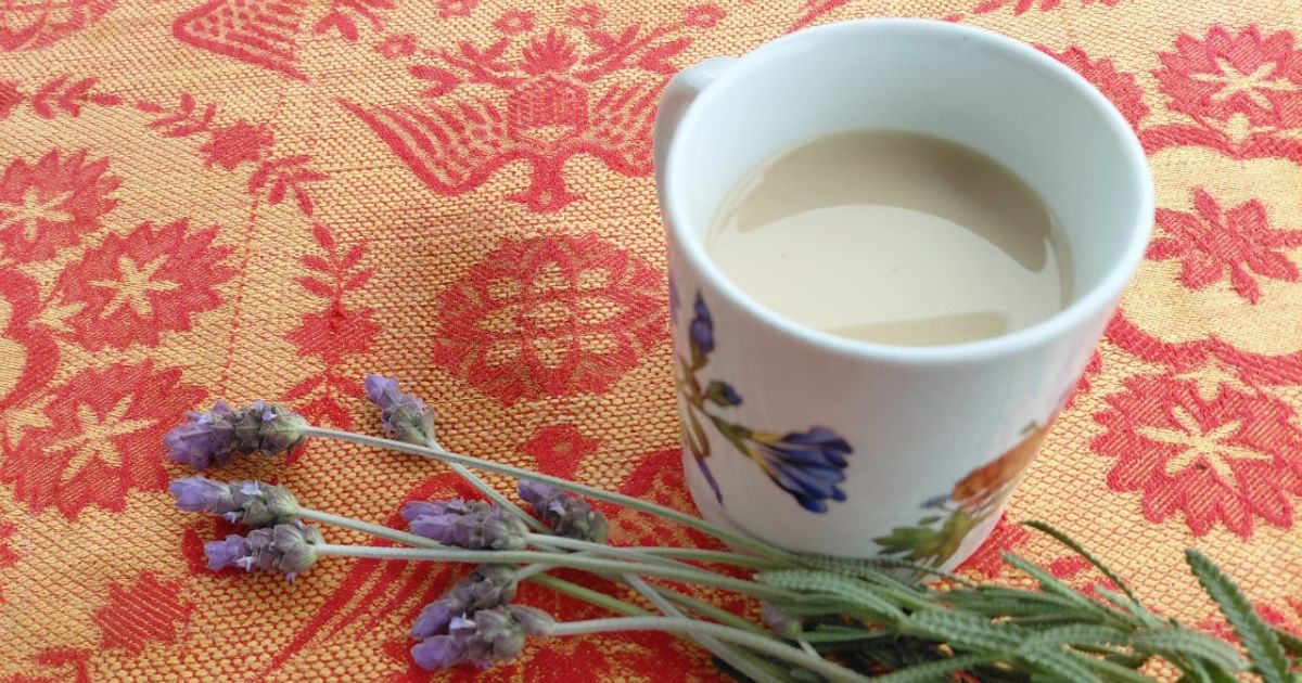 teacup filled with Chai tea on orange flowered tablecloth and fresh lavender along side.